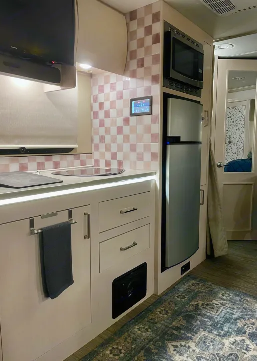 Explore this RV rental's sleek kitchen: microwave, fridge, induction cooktop, and checkered backsplash. TV & smart control panel visible.. Renegade Custom Coaches Vienna 2021