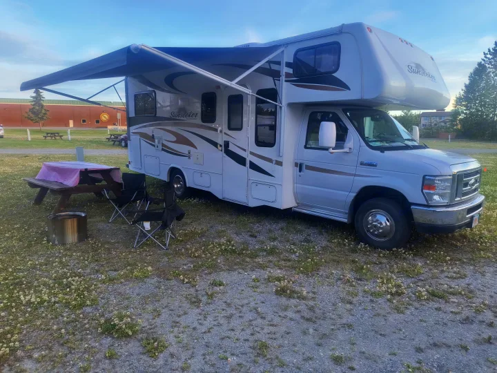 White Sunseeker RV rental parked at a campsite, with an extended awning, picnic table, and chairs for outdoor relaxation.. Forest River Sunseeker 2012