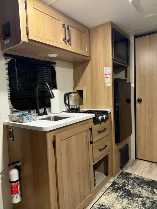 Inside an RV rental, featuring a modern kitchen with light wood cabinetry, sink, stovetop, microwave, and fridge.. Coleman Light 17BX 2025