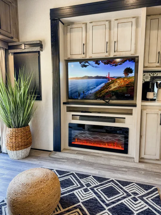 An RV rental interior featuring a TV, electric fireplace, modern light-wood cabinetry, and cozy accents.. Durango Gold 2023
