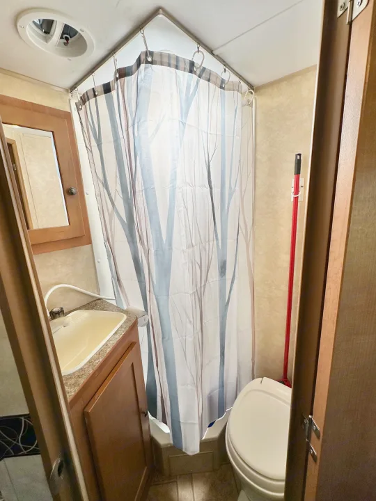 Compact RV rental bathroom features corner shower with tree-pattern curtain, toilet, and sink.. Cruiser RV Fun Finder X 2011