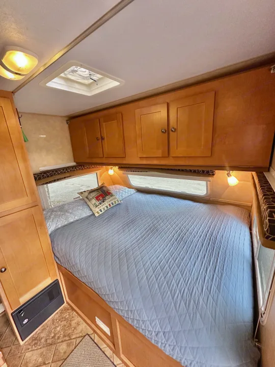 Comfortable RV rental bedroom featuring a quilted bed, overhead wooden cabinets, and a ceiling skylight.. Cruiser RV Fun Finder X 2011