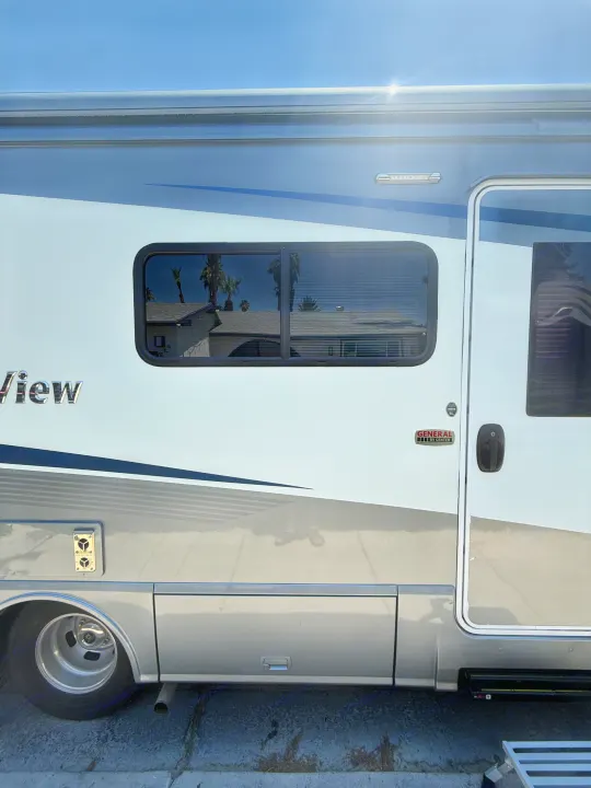 Side view of a white and grey RV, with a window reflecting palm trees, ready for your RV rental.. Winnebago View 24J 2020