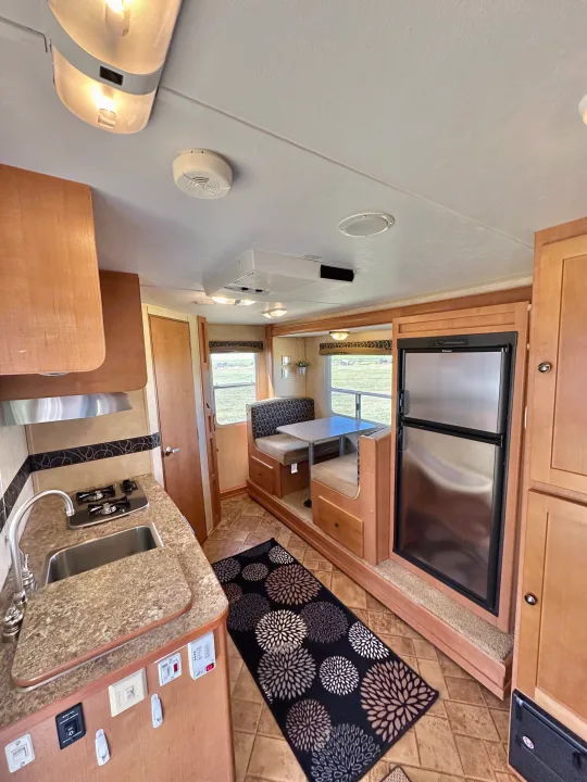 Cozy RV rental interior featuring a kitchen, dining booth, and refrigerator, ideal for travel adventures.. Cruiser RV Fun Finder X 2011
