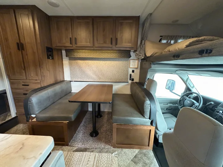 An RV rental's inviting interior featuring a dinette with grey upholstered benches, a front bunk bed, and wood cabinets.. Forest River Sunseeker LE 2021