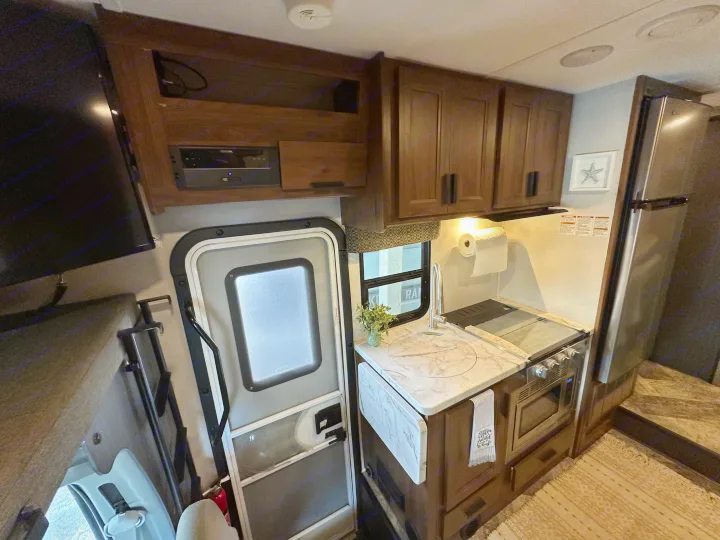 RV rental kitchen and living area, complete with sink, stove, fridge, and main door. Cozy camper interior ready for travel.. Forest River Sunseeker LE 2021