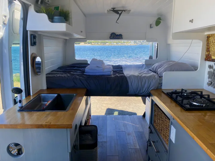 Spacious and cozy RV rental interior with ocean view bed, full kitchen, and stylish design, perfect for van life adventures.. Ram Promaster 2014