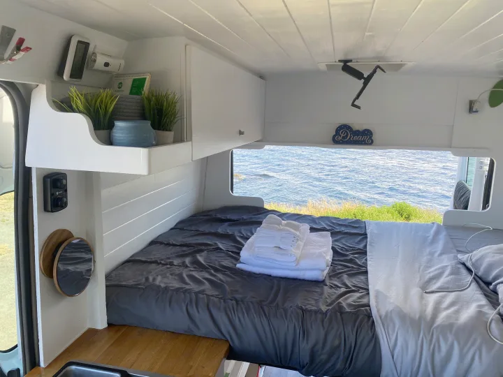 Cozy RV rental interior with a bed, ocean view, and clever storage. Perfect for a comfortable travel experience.. Ram Promaster 2014