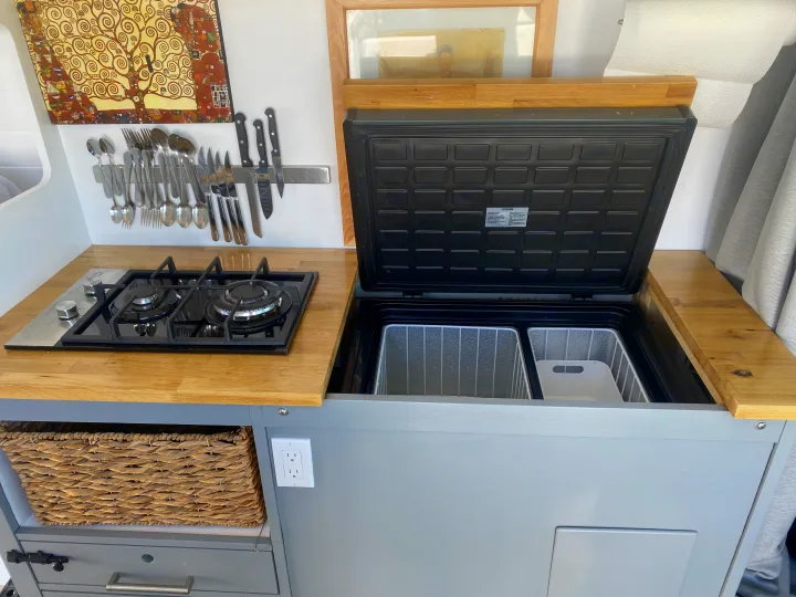 RV rental kitchen: 2-burner stove, magnetic utensil rack, open fridge/freezer, & wood counters. Compact mobile cooking.. Ram Promaster 2014