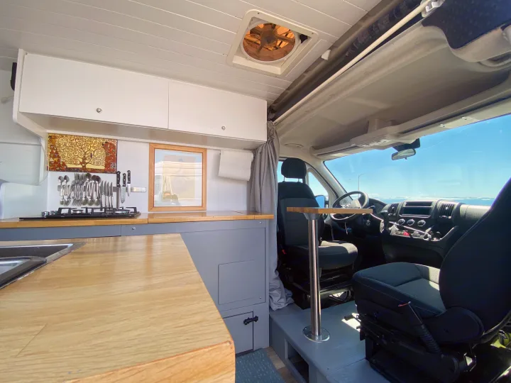 RV rental interior: A bright, functional camper van kitchen with a stove, sink, and dining table leading to driver seats.. Ram Promaster 2014