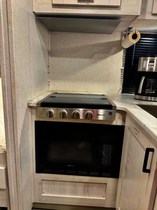 This RV rental kitchen features a Magic Chef stove, microwave, and Cuisinart coffee maker, ideal for cooking.. Entrada Entrada Motorhome 2022