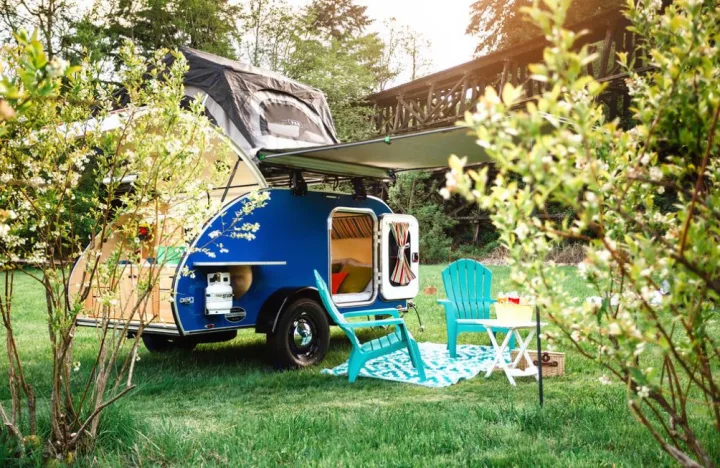 Vibrant blue teardrop RV rental features a rooftop tent, awning, and comfy outdoor seating with teal chairs for glamping.. Aero Steel 2021