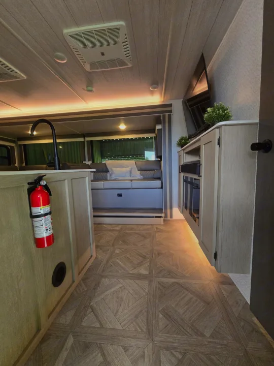 Modern RV rental interior: Kitchen with faucet & fire extinguisher, cozy living area, TV unit, wood floor.. Forest River Salem Cruise Lite Platinum 2023