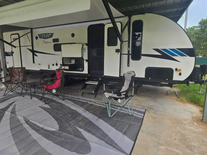 RV rental setup: white travel trailer with extended awning, outdoor rug, and camping chairs under a covered spot.. Forest River Salem Cruise Lite Platinum 2023