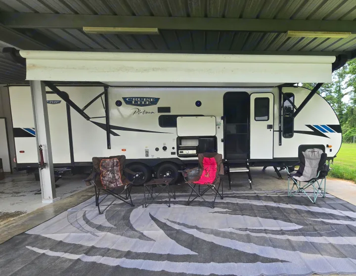 Spacious white rv rental under a carport with extended awning, outdoor kitchen, and cozy chairs on a patterned rug.. Forest River Salem Cruise Lite Platinum 2023