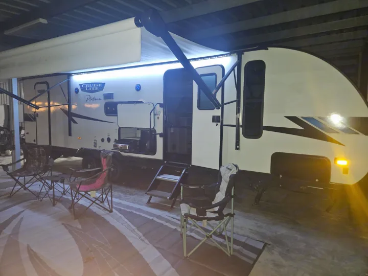 Cozy RV rental setup at night: travel trailer with illuminated awning, pull-out grill, and camping chairs.. Forest River Salem Cruise Lite Platinum 2023