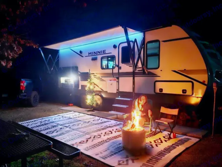 An RV rental setup at night: a lit Winnebago Minnie, a person by a fire pit, and a patterned rug.. Winnebago Minnie 2201MB 2022