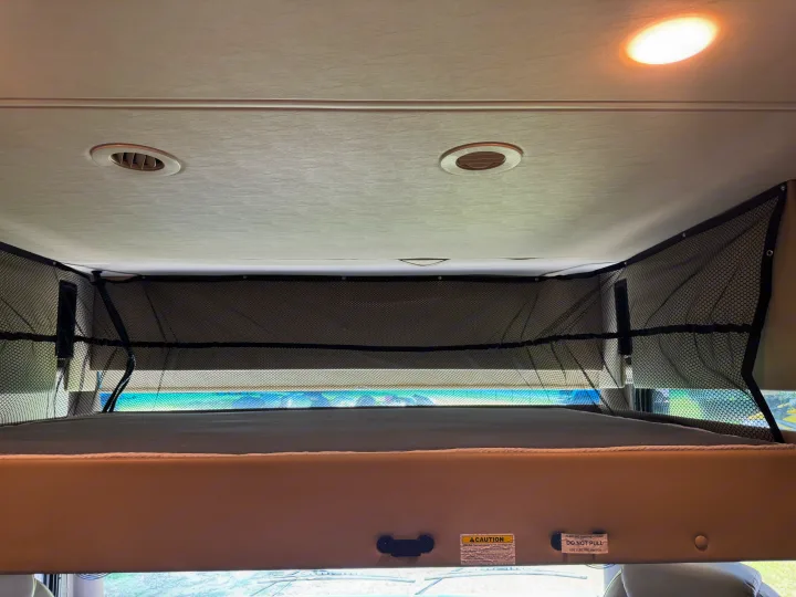 Overhead bunk bed with safety net in an RV rental, showing 500 lbs. weight capacity and electric switch warnings.. Thor Challenger 2020