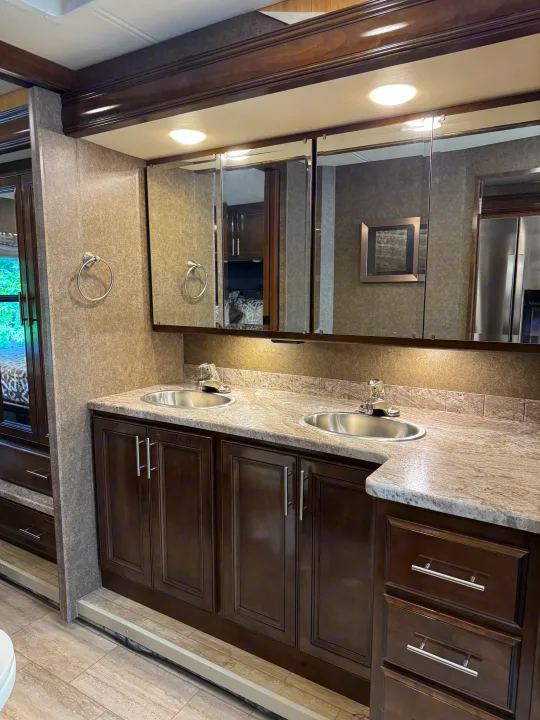 Modern RV rental bathroom: double vanity with dark wood cabinets, dual sinks, and lighted mirrors.. Thor Challenger 2020