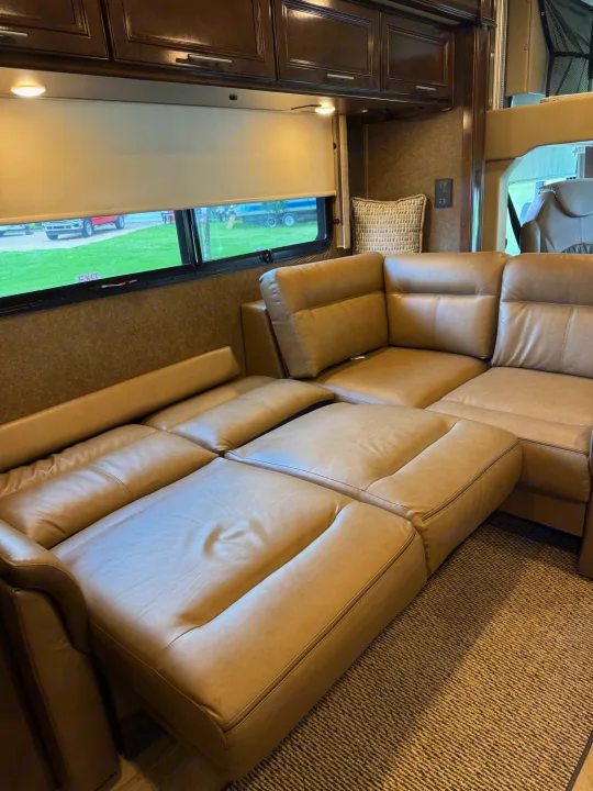 This RV rental's living space features a large, light brown leather sectional with extended recliners and overhead cabinets.. Thor Challenger 2020