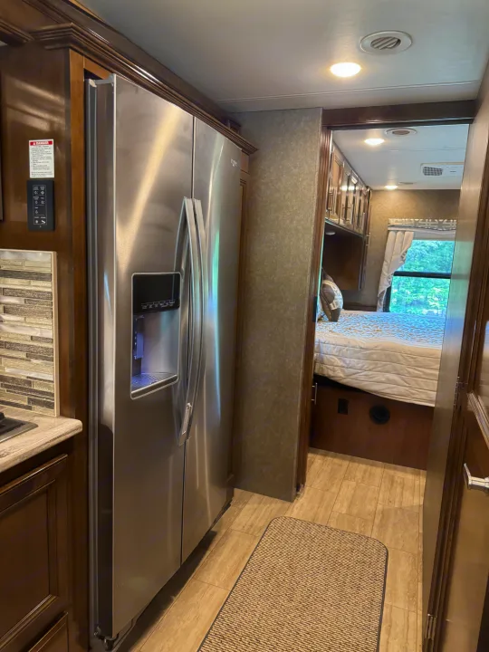 Experience comfort in this RV rental: modern kitchen with a stainless steel fridge, leading to a cozy bedroom.. Thor Challenger 2020