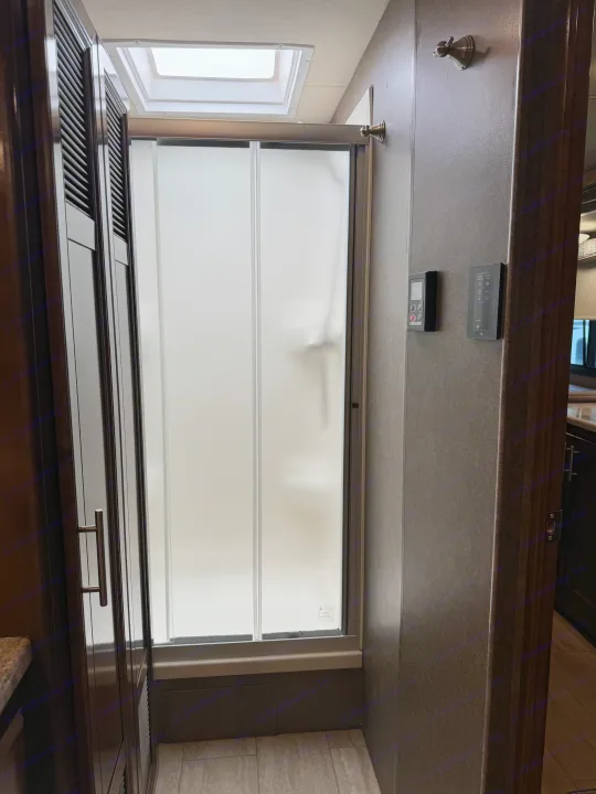 RV rental bathroom features a frosted glass shower stall, dark wood cabinets, and a skylight, providing natural light.. Thor Challenger 2020