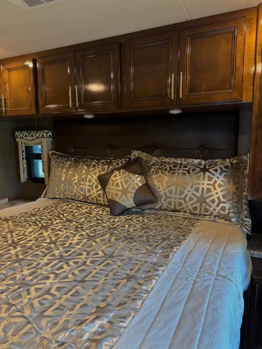 Inviting RV rental bedroom with modern bedding, dark wood cabinets, and padded headboard, ideal for comfortable travel.. Thor Challenger 2020