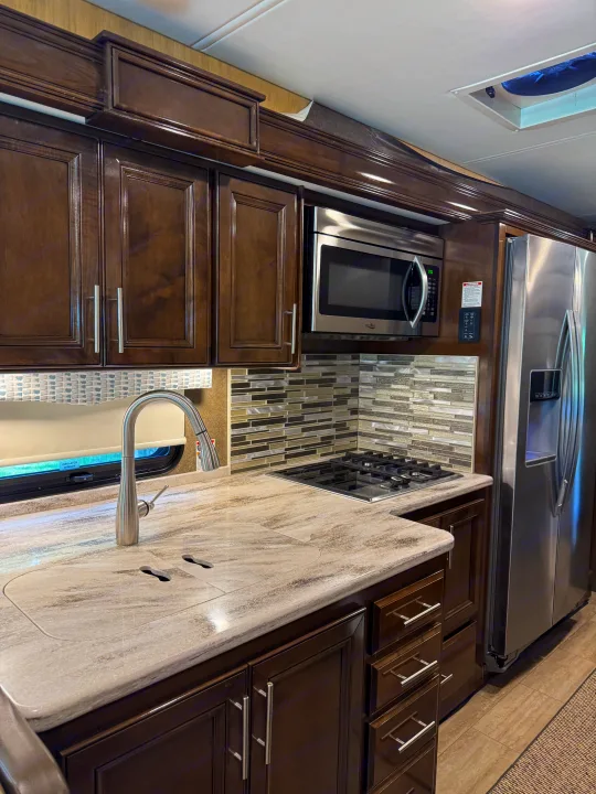 Inside an RV rental: a well-appointed kitchen with dark cabinets, modern appliances, and a tiled backsplash.. Thor Challenger 2020