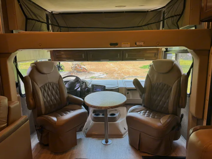 Spacious RV rental interior featuring the cockpit with two comfortable chairs, a small table, and an overhead bunk. Ready for adventure!. Thor Challenger 2020