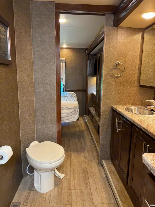 Compact RV rental bathroom with toilet, sink, and view into the cozy bedroom.. Thor Challenger 2020