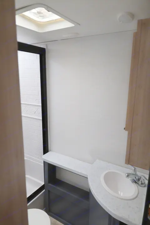 Modern RV rental bathroom interior with a tiled shower, vanity sink, and overhead light/skylight. Clean and functional.. Forest River Tracer 28BHS 2024