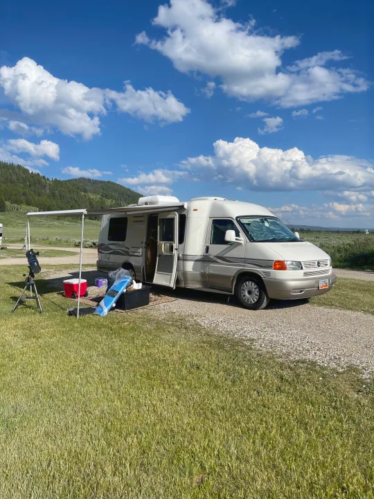 RV rental parked at a scenic campsite with its awning extended and a telescope set up for stargazing.. Eurovan Camper Rialta 2000