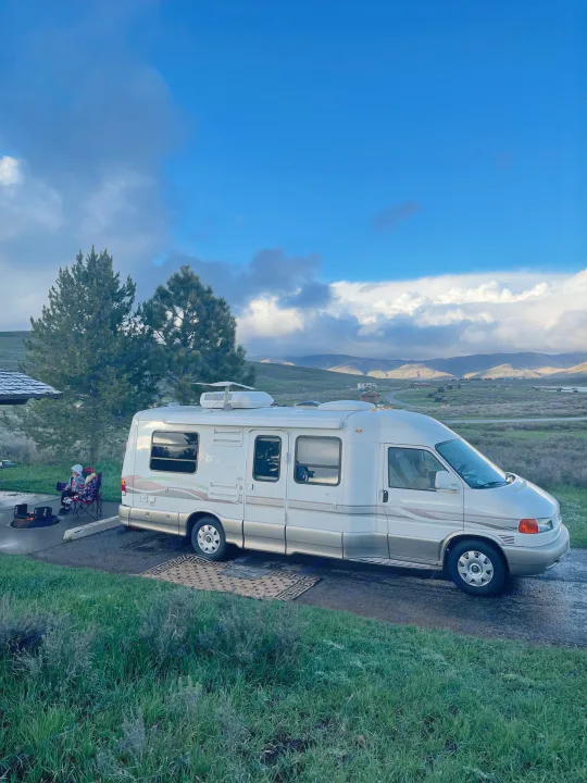 Scenic RV rental camping: A camper van is parked with a child & dog, fire pit, mountains & clouds.. Eurovan Camper Rialta 2000