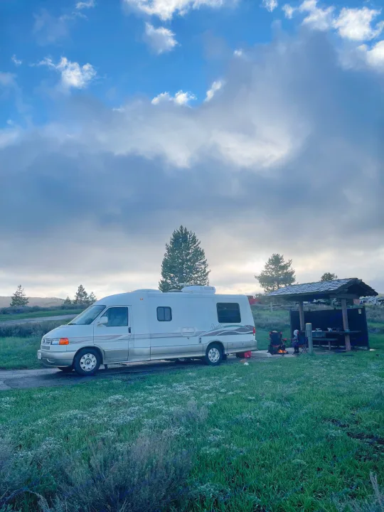 White RV rental parked at a frosty campsite next to a picnic shelter and warm campfire under a cloudy sky.. Eurovan Camper Rialta 2000