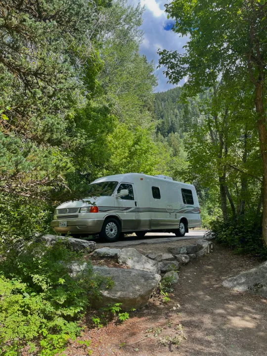 Experience the outdoors! This white Rialta camper van, ideal as an rv rental, is parked on a road amidst lush trees and mountains.. Eurovan Camper Rialta 2000