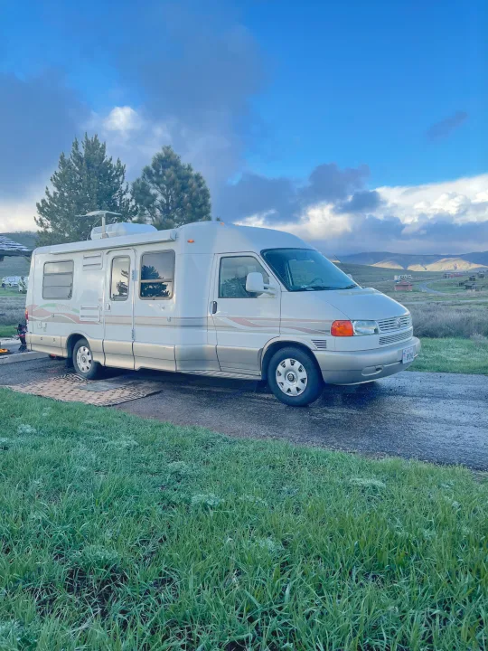 Experience outdoor adventure with an RV rental! This white camper van is parked at a scenic campground with mountains.. Eurovan Camper Rialta 2000