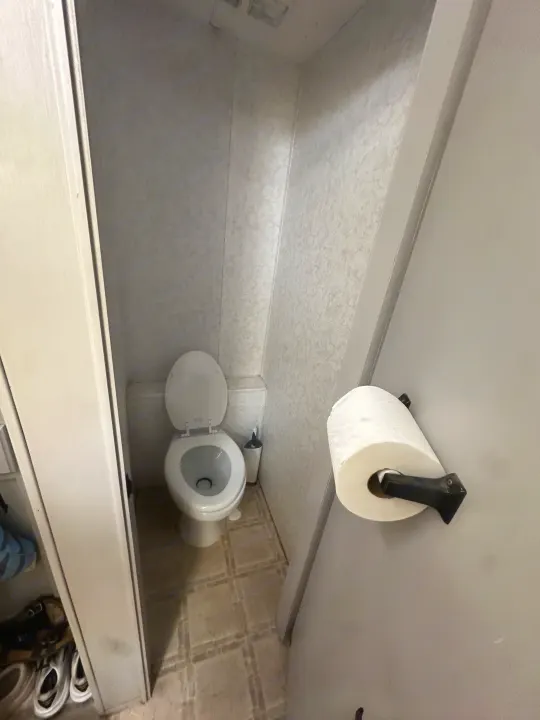 Compact toilet area inside an RV rental, showing the toilet, brush, and toilet paper on the door. Typical compact design.. Thor Motor Coach Tahoe 2003