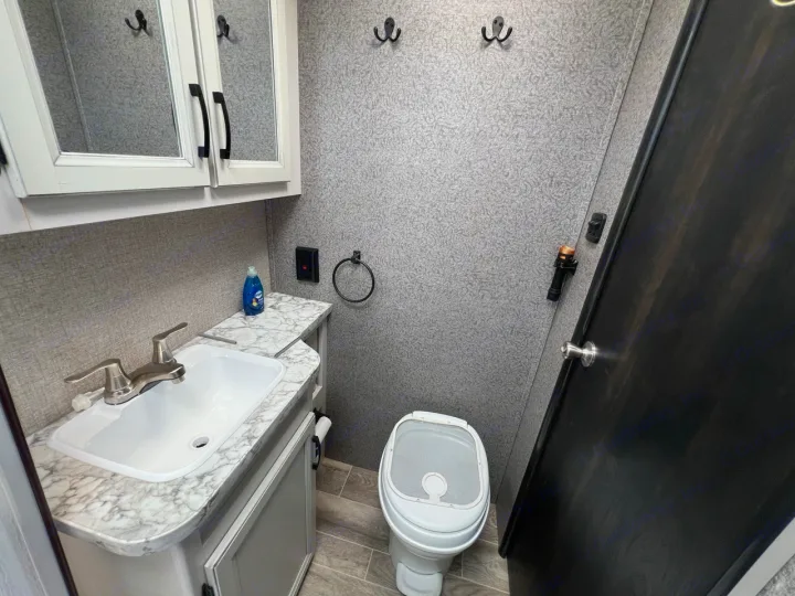 Inside an RV rental bathroom: a compact sink, toilet, and storage cabinets in light gray and white finishes.. Jayco Jay Feather Micro 2021