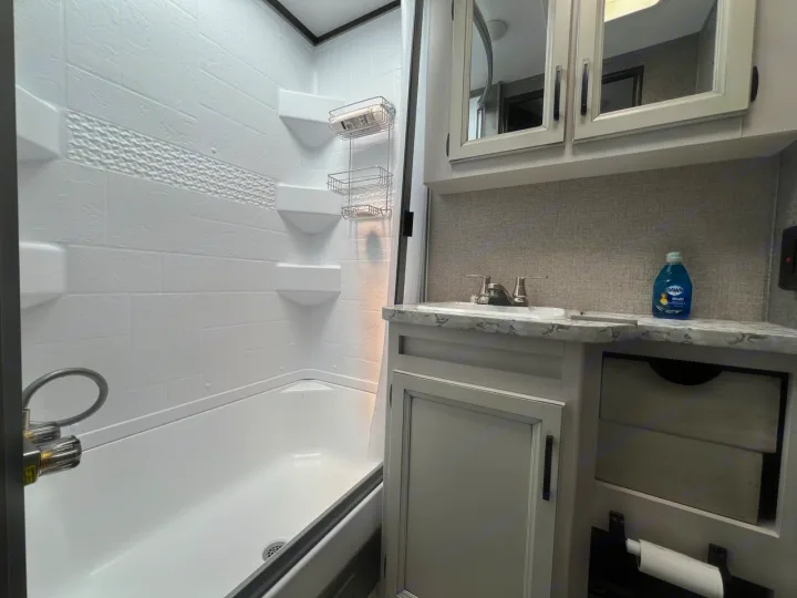 Inside an RV rental bathroom: a bright white shower/tub combo is on the left, while a light-toned vanity and sink are on the right.. Jayco Jay Feather Micro 2021