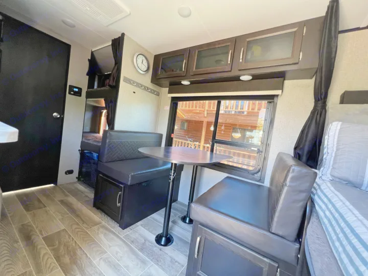 RV rental interior featuring a modern dinette, overhead cabinets, window views, and bunk beds, with a cozy main bed to the right.. Jayco Jay Feather Micro 2021