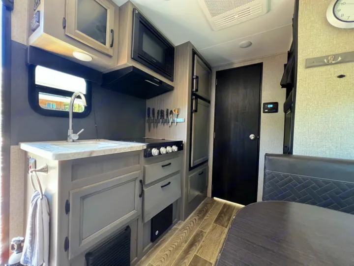 Step into a modern RV rental kitchen: sink, microwave, stove, fridge, and dining area. Features stylish gray cabinets & wood-look floor.. Jayco Jay Feather Micro 2021