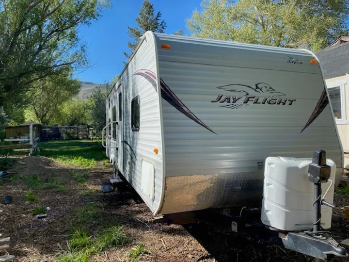 White Jayco RV rental travel trailer outdoors. Bright day, green yard, mountains visible in background.. Jayco Jay Flight 2013