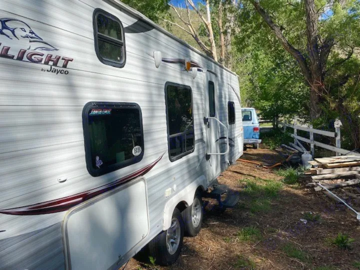 This RV rental, a Jayco travel trailer, sits in a rustic outdoor setting with a blue van and trees in the background.. Jayco Jay Flight 2013