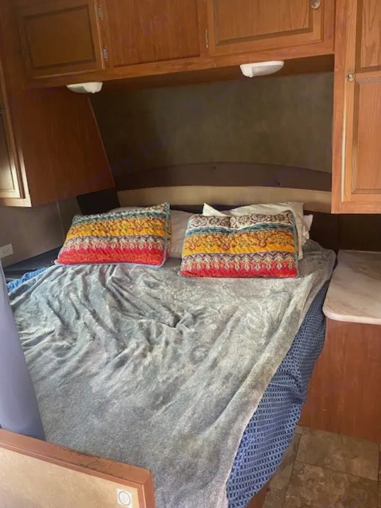 Cozy RV rental bedroom featuring a comfortable bed with colorful pillows, a plush grey blanket, and ample overhead storage.. Jayco Jay Flight 2013