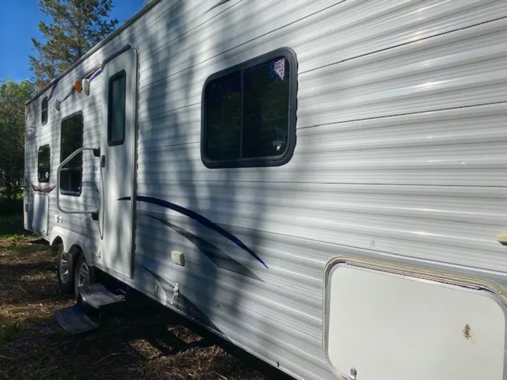 Side view of a white RV with ribbed siding, a closed door, extended steps, windows, and storage. Explore an rv rental trip!. Jayco Jay Flight 2013