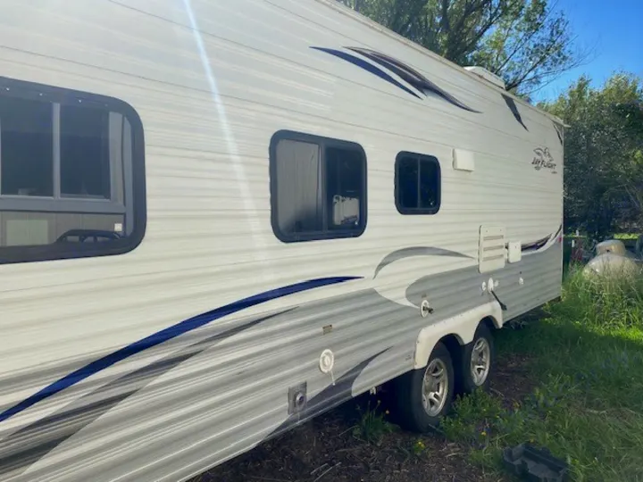 Side view of a white and grey Jay Flight travel trailer (RV) with blue accents, parked outdoors, ready for RV rental.. Jayco Jay Flight 2013