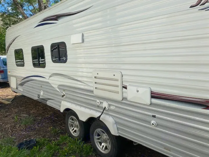 Explore with this white & grey RV rental. Side view of a travel trailer, featuring multiple windows and exterior utility panels.. Jayco Jay Flight 2013