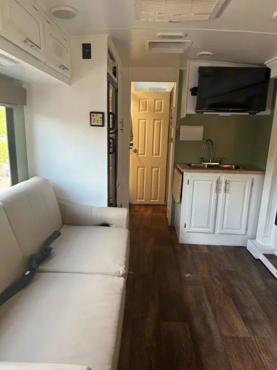 RV rental interior: a comfy white sofa, compact kitchen with sink, wall-mounted TV, & wood-look floor.. FR3 FR3 Motorhome 2016