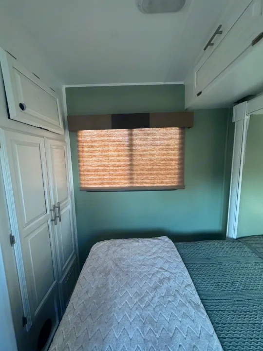 Clean RV rental bedroom featuring white cabinets, sage green walls, a window with a pleated shade, and cozy bedding.. FR3 FR3 Motorhome 2016
