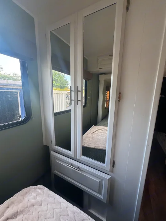 Cozy RV rental bedroom featuring a mirrored wardrobe, a comfortable bed, and a window looking out to trees and buildings.. FR3 FR3 Motorhome 2016